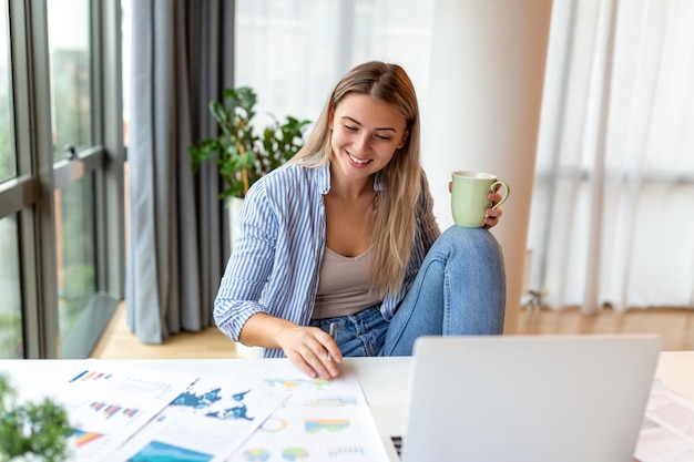 Remote job technology and people concept happy smiling young business woman with laptop computer and papers working at home office