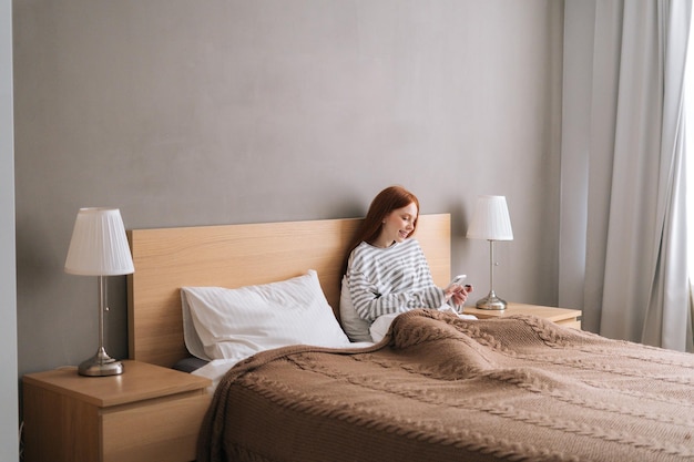 Remote view of happy young woman enjoy shopping online with credit card and mobile phone lying in bed at home