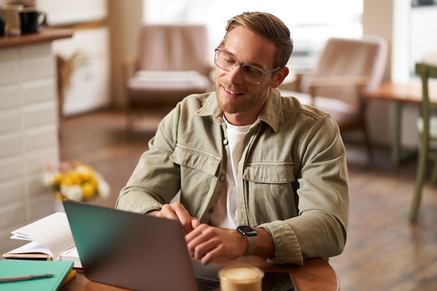 Remote work and freelance concept handsome man in glasses sits with notebook and laptop studying