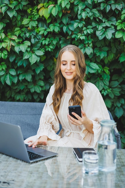 Remote work of a freelancer woman on a summer terrace on a laptop A businesswoman in a dress drinks water and works on a laptop