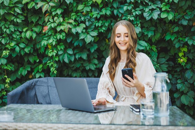 Remote work of a freelancer woman on a summer terrace on a laptop A businesswoman in a dress drinks water and works on a laptop