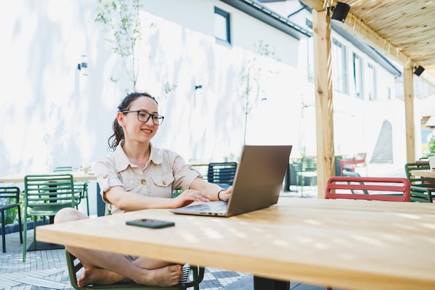 Remote work Relaxed woman sitting on outdoor terrace in cafe and working online with coffee and phone Female freelancer works remotely online while sitting in a summer cafe at a laptop