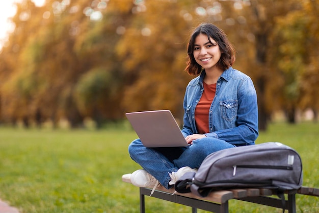 Remote Work Smiling Young Arab Woman Sitting With Laptop On Bench Outdoors