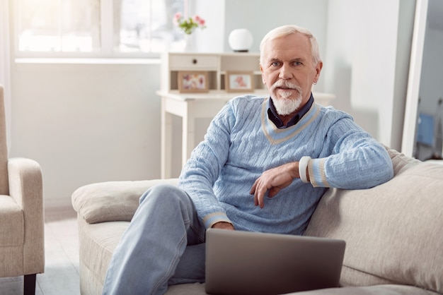 Remote worker. Handsome senior man posing while sitting on the couch and using his laptop, working on it