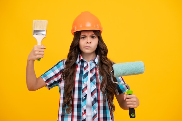 Renovation for childrens room Little girl in protective helmet and paint brush for painting walls Serious teenager girl