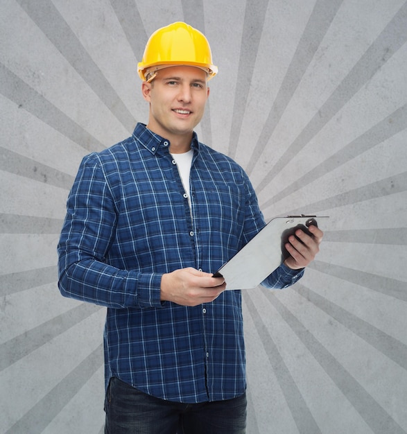 repair, construction, building, people and maintenance concept - smiling male builder or manual worker in helmet with clipboard over gray burst rays background