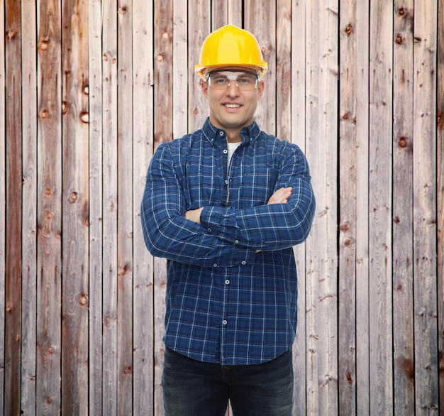 repair, construction, building, people and maintenance concept - smiling male builder or manual worker in helmet over wooden fence background