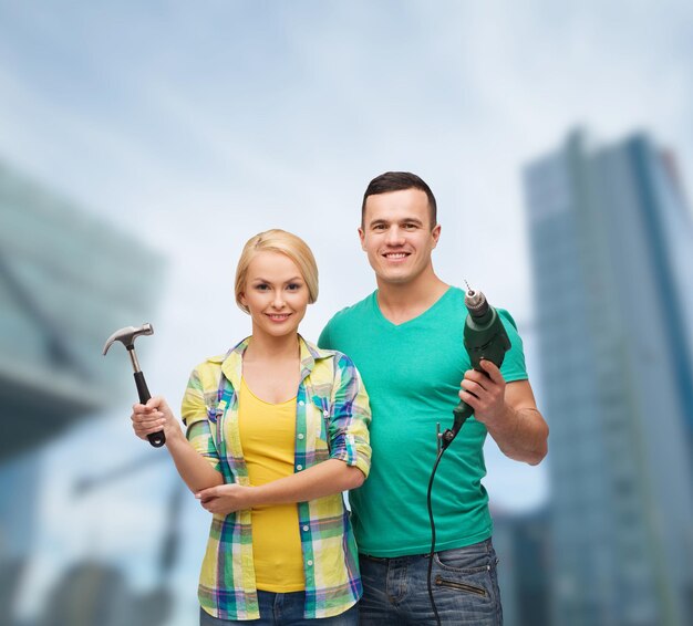 repair, construction and maintenance concept - smiling couple with hammer and drill over white background