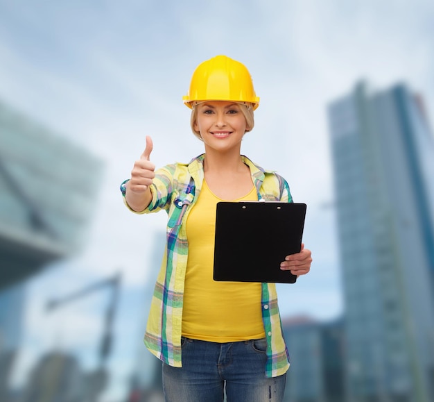 repair, construction and maintenance concept - smiling woman in helmet with clipboard showing thumbs up