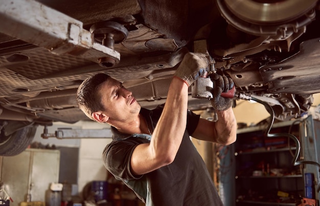 Repair man fixing car in repair station under lifted car during repair in garage