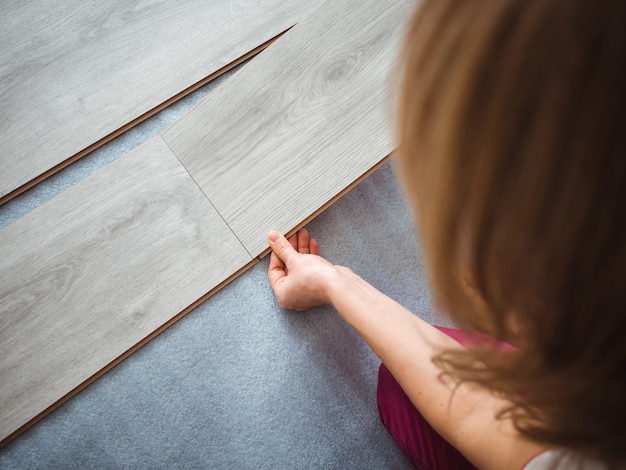 Photo the repair process in the apartment. the girl puts the laminate on the floor. back view