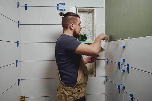 Repairman applying tile adhesive with a trowel on the bathroom wall