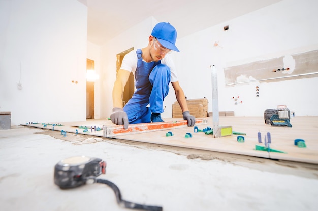 Repairman in grey gloves and uniform laying tiles with tile leveling system on the floor in house