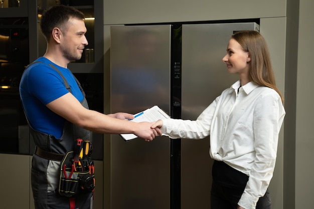 Repairman shows fixed refrigerator to woman in kitchen