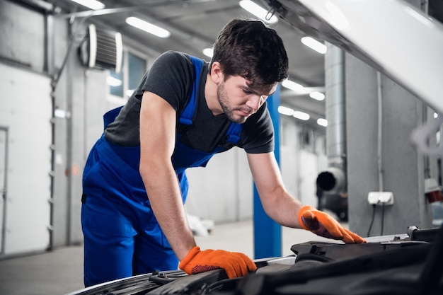 Repairman in working gloves opened the hood of the car and checks the engine