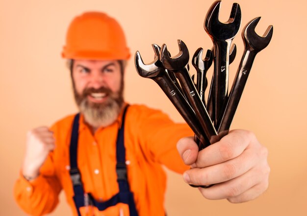 Photo repairment tools. smiling worker with wrenches. builder in construction helmet with spanners. selective focus.