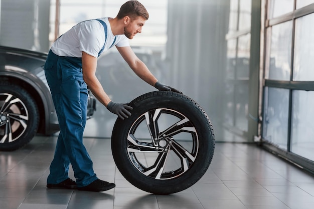 Replacement of wheel Young man in white shirt and blue uniform repairs automobile