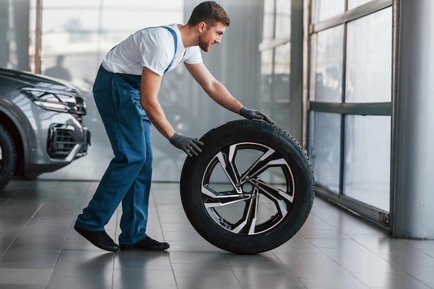 Replacement of wheel Young man in white shirt and blue uniform repairs automobile