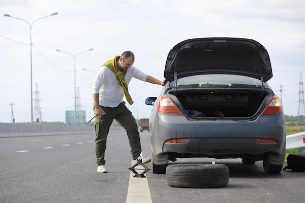 Replacing the wheel of a car on the road. A man doing tire work on the sidelines.