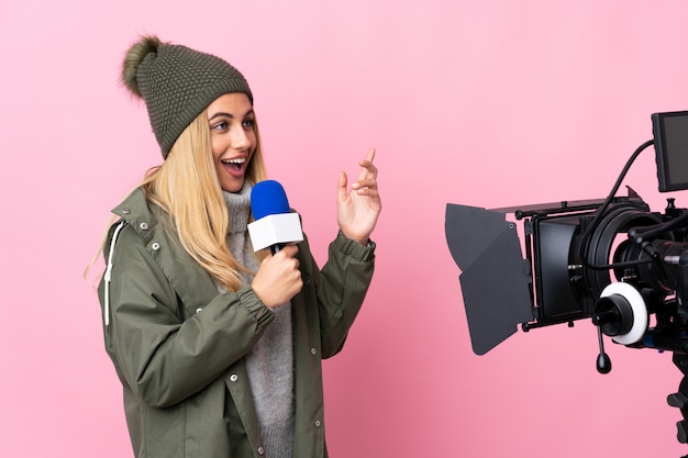 Reporter woman holding a microphone and reporting news over isolated pink