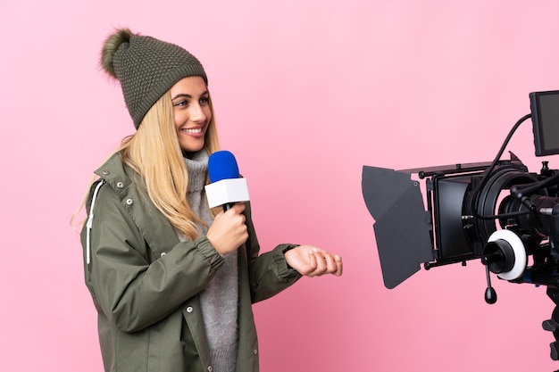 Reporter woman holding a microphone and reporting news over isolated pink