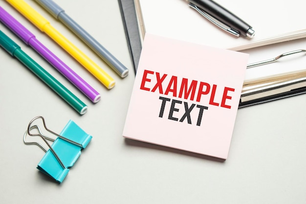 Photo reports and color charts are on the table. there are also red pens, pencil and paper in a black frame with the words example text. view from above