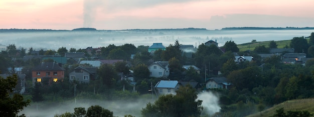 Residential cottages among green trees covered with blue fog