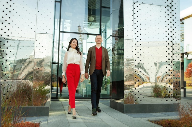 Respectable businessman and fashionable asian business woman walking near office full length