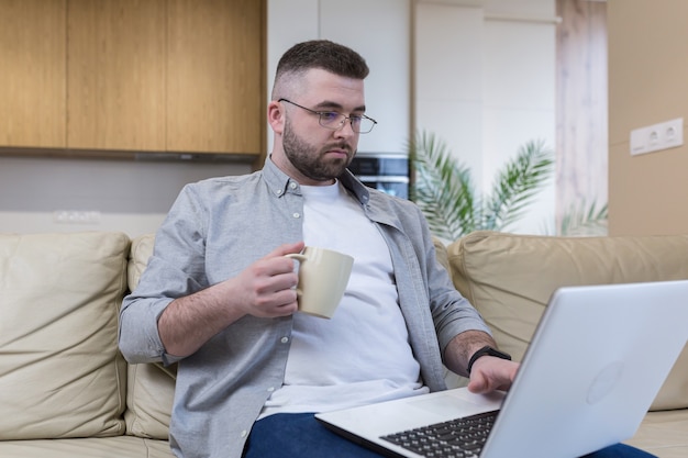 respectable handsome man working from home office sitting on sofa with laptop and solving business case