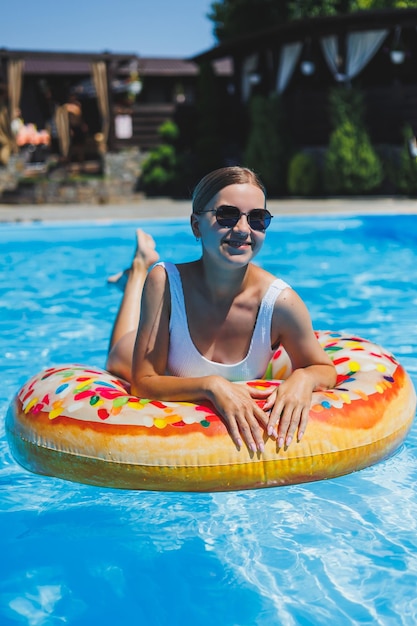 Rest in the pool Happy young woman in swimsuit sunglasses and inflatable rubber ring floating in blue water Summer luxury holidays in the spa resort pool