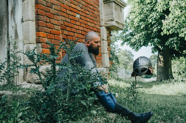 Photo rest of viking warrior near an old brick castle and tall tree sword and helmet