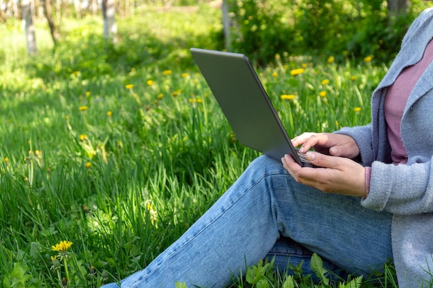 Rest with a laptop in nature in the park on a sunny day against the backdrop of green grass