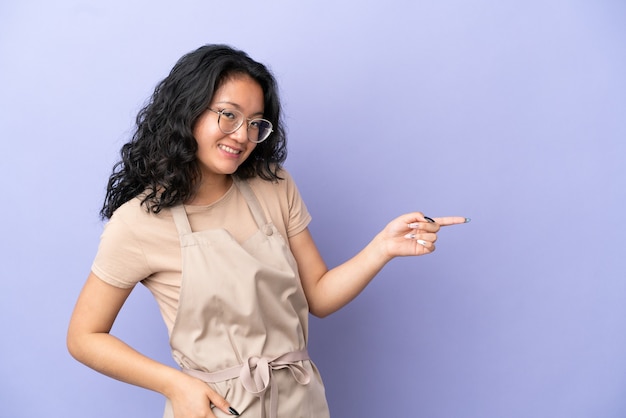 Restaurant asian waiter isolated on purple background pointing finger to the side and presenting a product