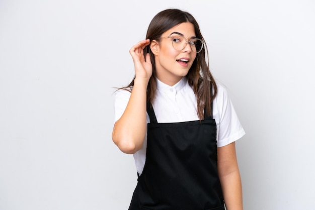 Restaurant Brazilian waiter woman isolated on white background listening to something by putting hand on the ear