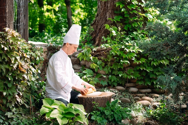 A restaurant chef in uniform rolls out dough on a stump in the woods