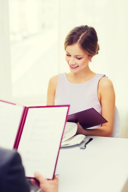 restaurant, couple and holiday concept - smiling young woman looking at menu at restaurant