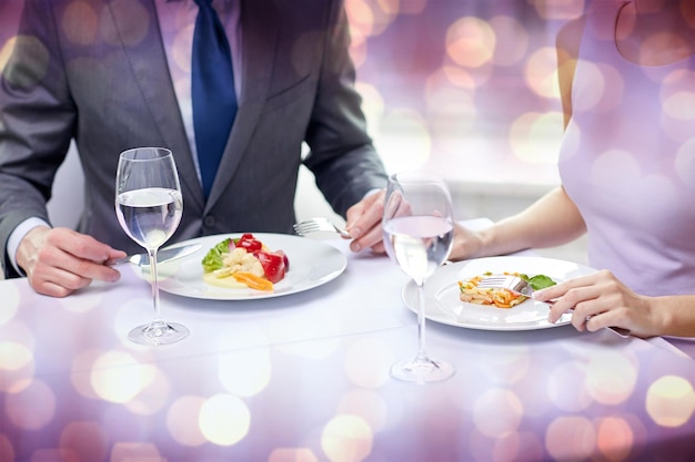 restaurant, food, people, date and holiday concept - close up of couple eating appetizers at restaurant over violet holidays lights background