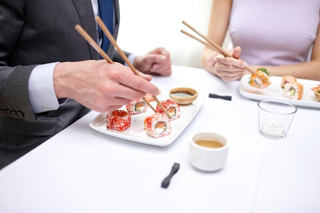 restaurant, food, people, date and holiday concept - close up of couple eating sushi at restaurant