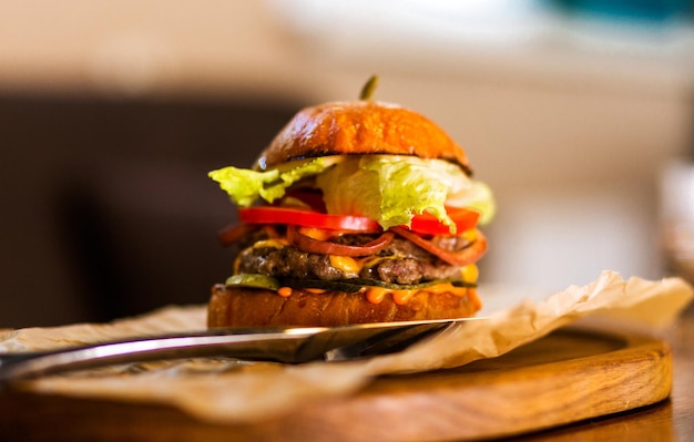 The restaurant has a burger with beef cheese sauce fresh tomatoes and salad on a wooden plateau Horizontal photo