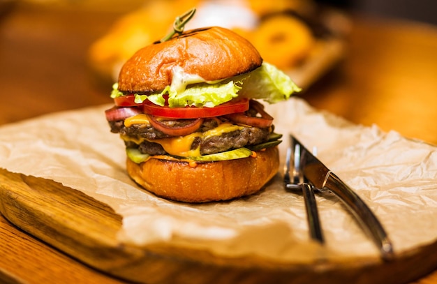 The restaurant has a burger with beef cheese sauce fresh tomatoes and salad on a wooden plateau Horizontal photo