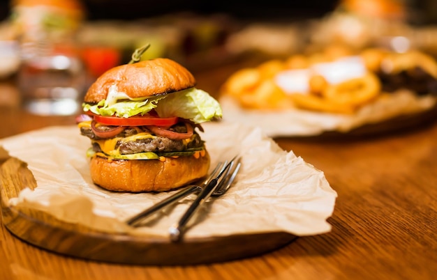 The restaurant has a burger with beef cheese sauce fresh tomatoes and salad on a wooden plateau