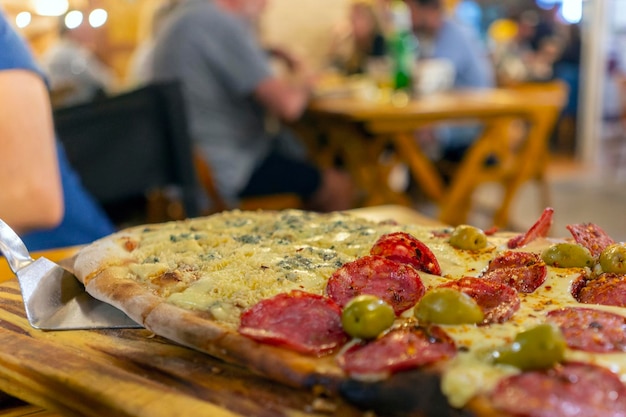 Restaurant pizza in pieces with salami and olives on wooden plate