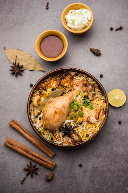 Restaurant style Spicy Chicken Biryani in wooden bowl with Raita and salan, Popular Indian or Pakistani Food