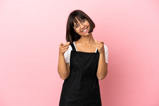 Restaurant waiter over isolated pink background pointing front with happy expression