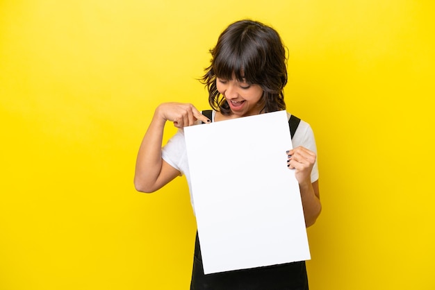 Restaurant waiter latin woman isolated on yellow bakcground holding an empty placard with happy expression and pointing it