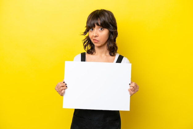 Restaurant waiter latin woman isolated on yellow bakcground holding an empty placard