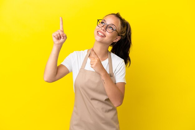 Restaurant waiter Russian girl isolated on yellow background pointing with the index finger a great idea