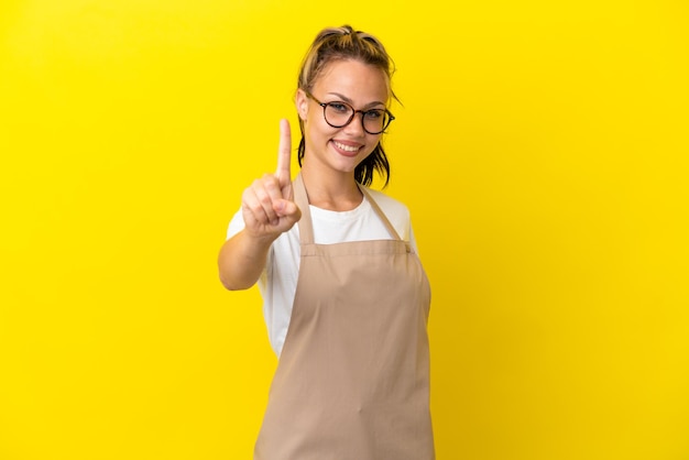 Restaurant waiter Russian girl isolated on yellow background showing and lifting a finger