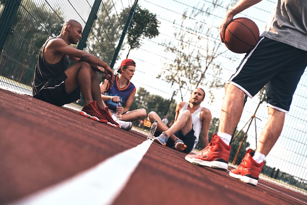 Resting after game. Group of young men in sports clothing resting while sitting on the basketball field outdoors