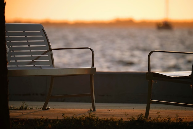 Resting bench in public park on sea shore at sunset